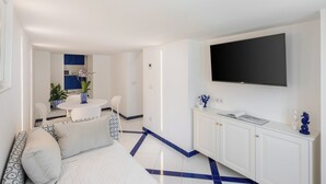 Una sala de estar moderna con un sofá, un televisor montado en la pared y una zona de comedor con mesa y sillas.