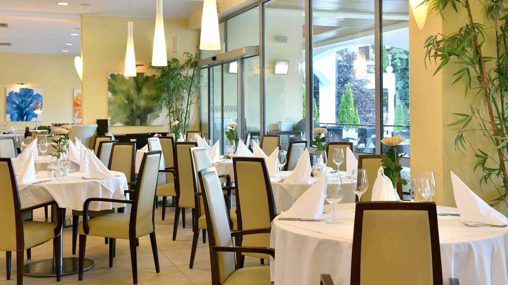 A restaurant with round tables, chairs, and hanging pendant lights.