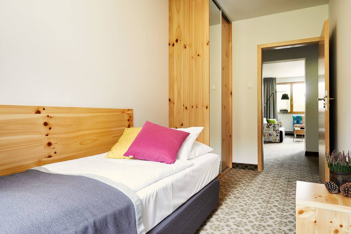 Une chambre à coucher avec une tête de lit en bois, un lit avec une literie blanche et rose, et une couverture grise.