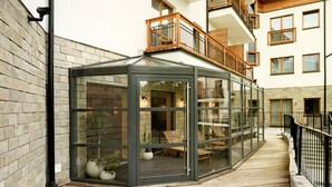 A conservatory with glass walls, wooden flooring, and a balcony with wooden railings.