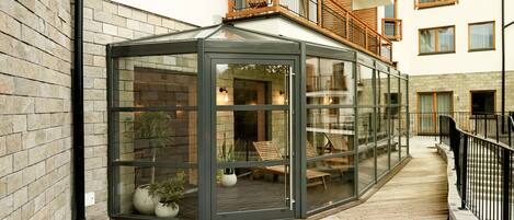 A conservatory with glass walls, wooden flooring, and a balcony with wooden railings.