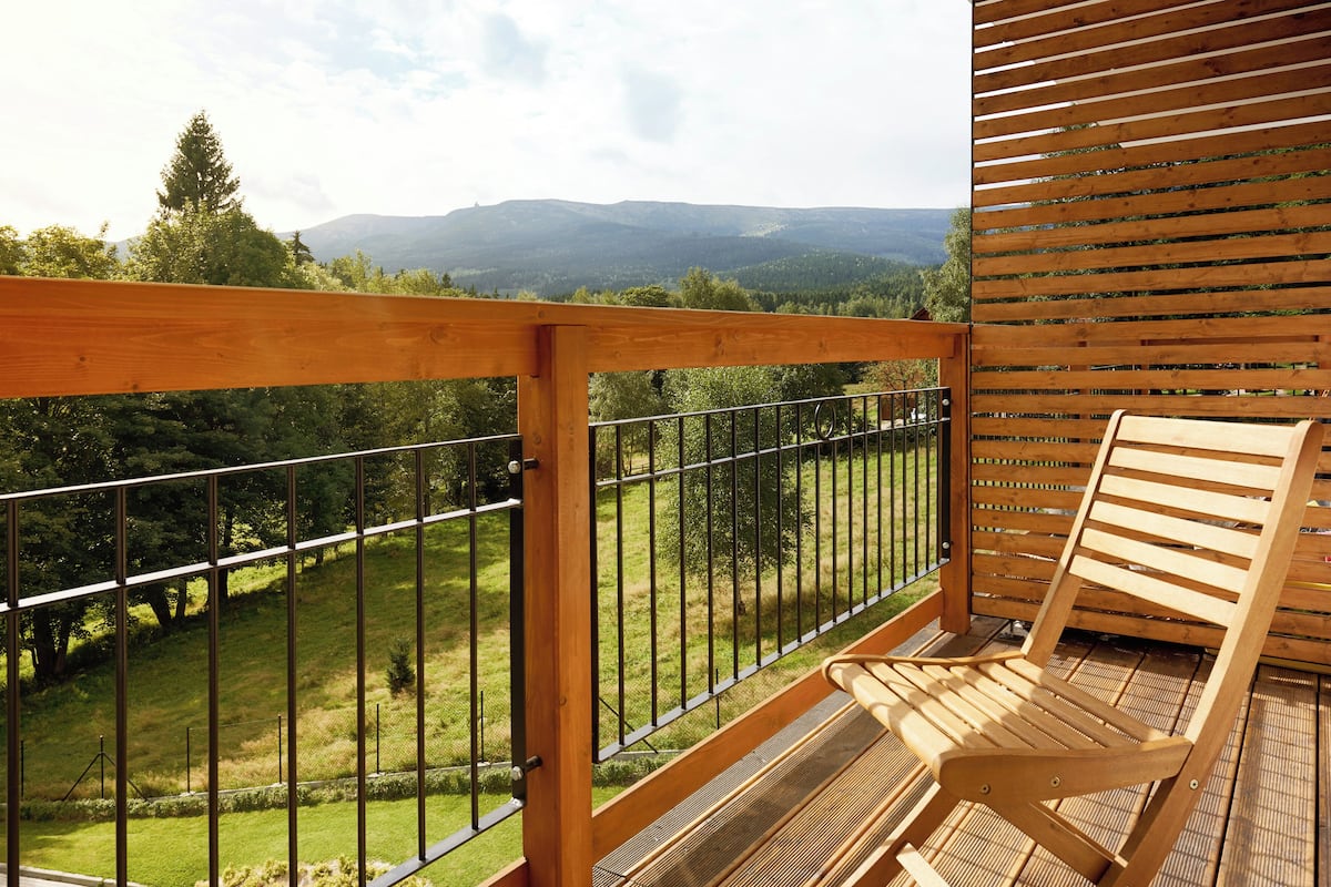 Une terrasse en bois avec une rambarde en métal, une chaise en bois et une vue sur un paysage montagneux.