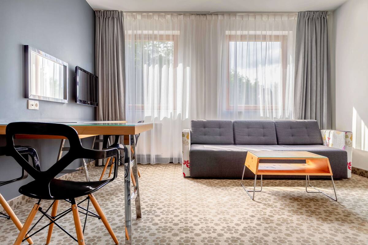 Un salon moderne avec un canapé gris, une table basse en bois, un fauteuil noir et un téléviseur fixé au mur.