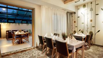 A dining area with a table set for six, wooden chairs, and a view through a glass door to an outdoor seating area.