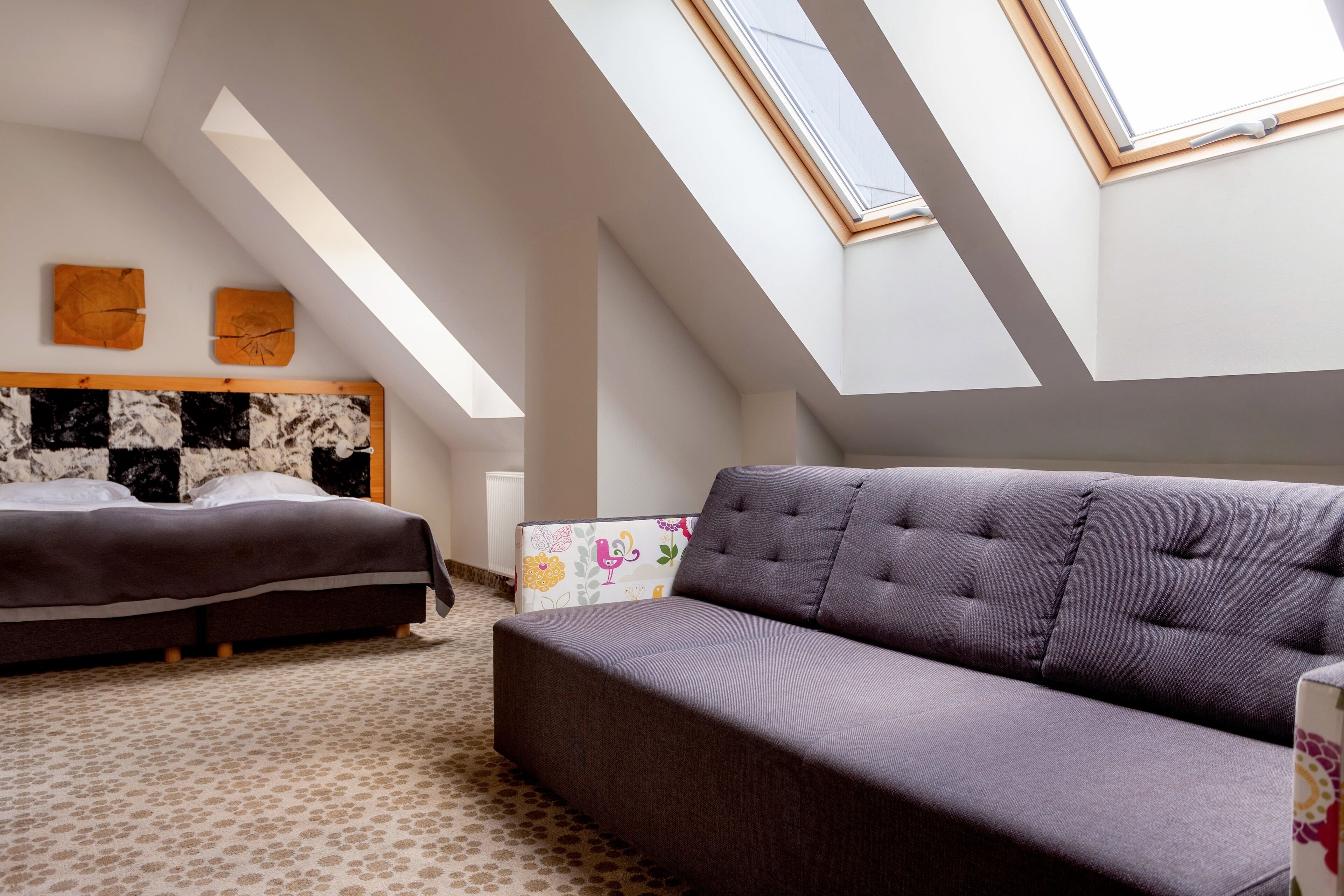 Un dormitorio con cama, sofá, cabecera estampada en blanco y negro, y tragaluz.