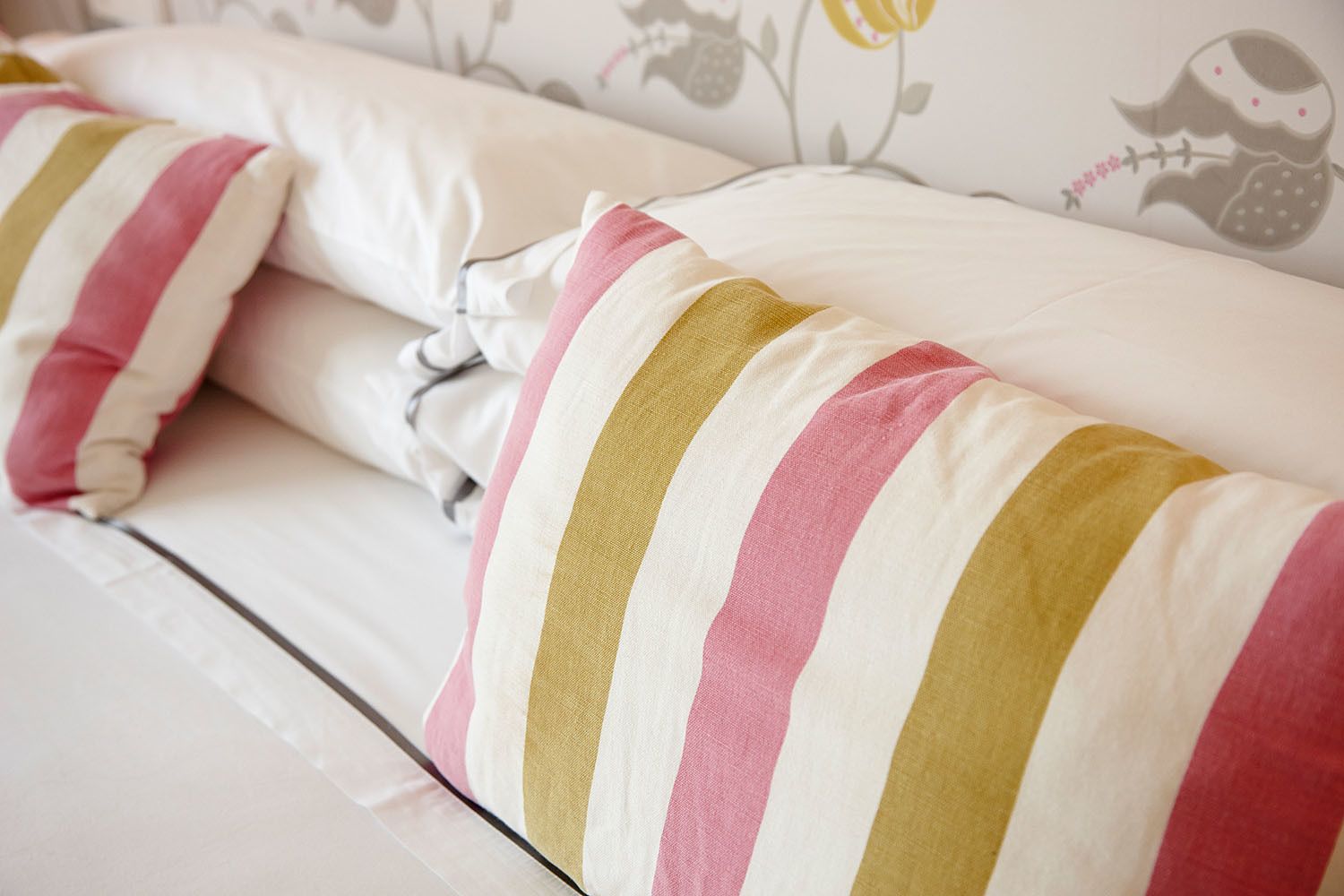 Een bed met gestreepte kussens en bloemenbehang.