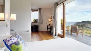 Een hotelkamer met een groot bed, een bureau met stoel, een bijzettafeltje met lamp, uitzicht op het omliggende landschap en een balkon met stoelen.
