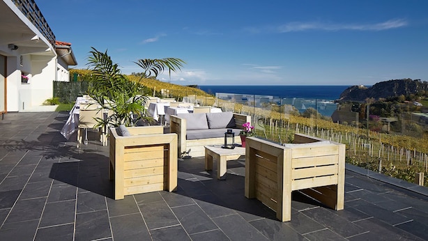Een terras buiten met houten meubels, een tafel en uitzicht op zee en wijngaarden.