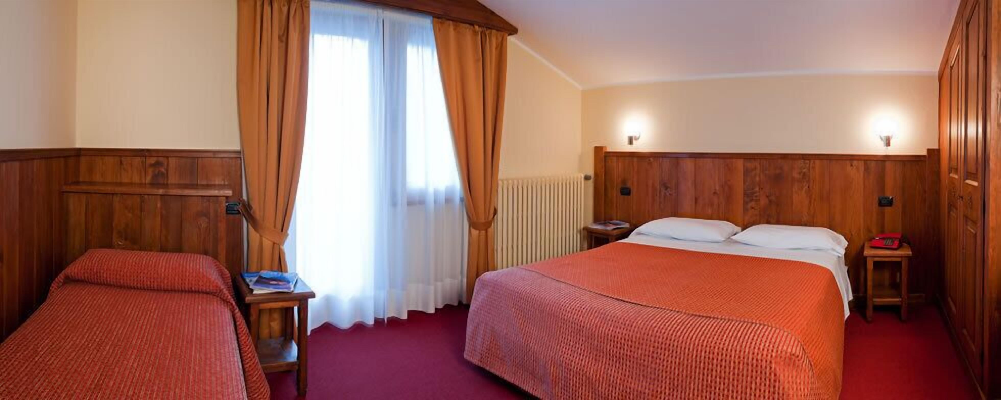 Een hotelkamer met twee bedden, houten lambrisering, een radiator en een raam met gordijnen.