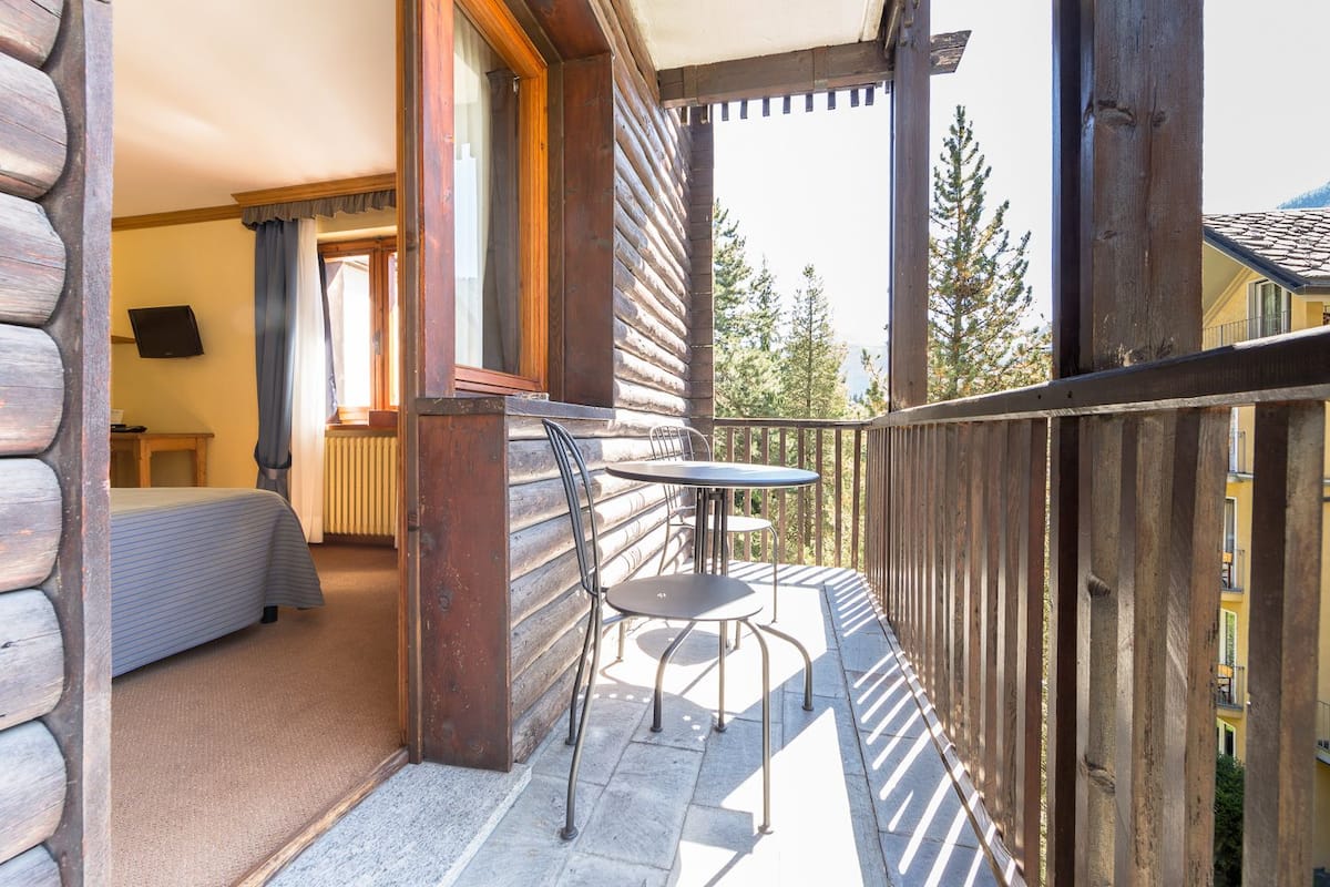 A wooden cabin with a balcony, a bed, and a table with chairs.