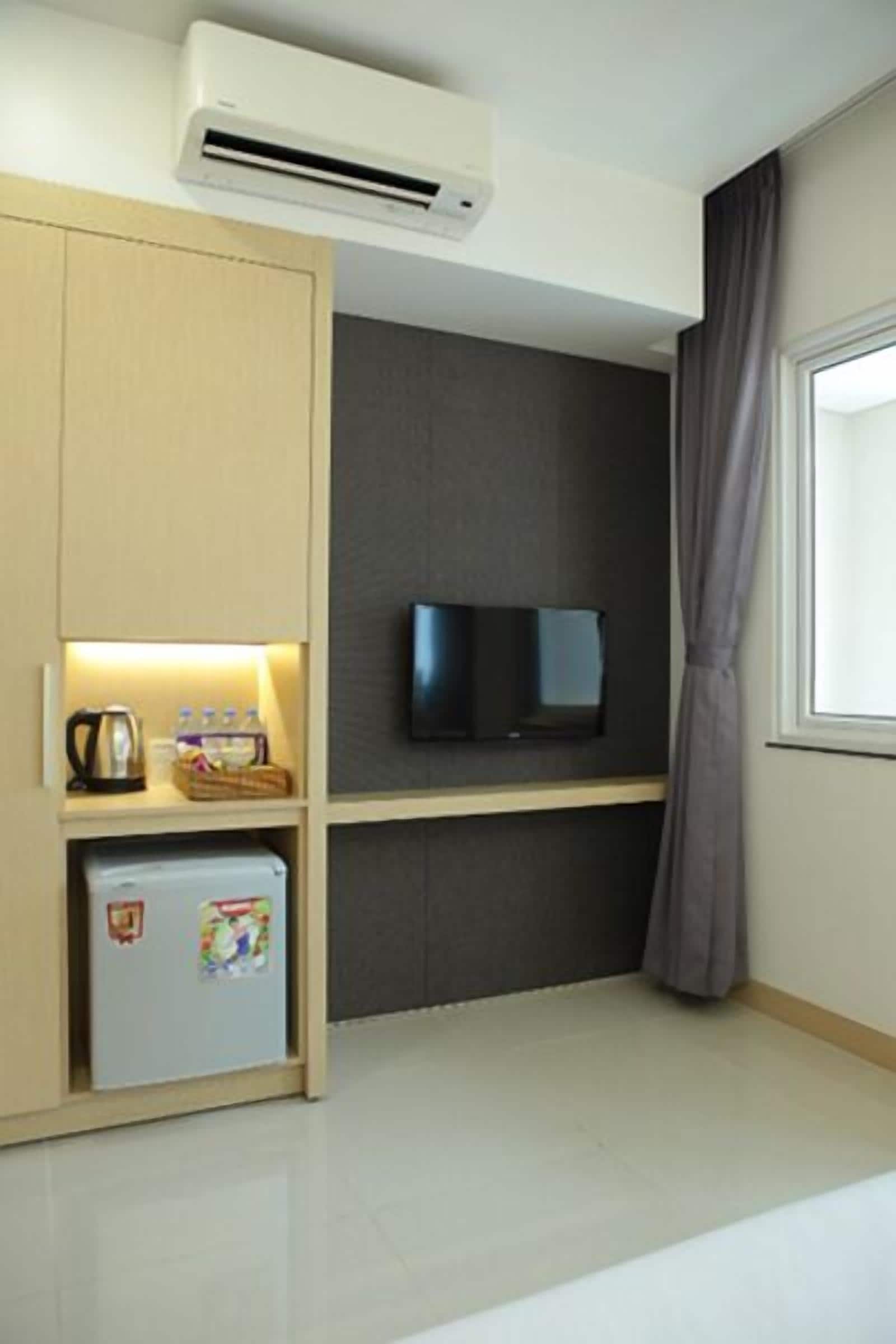 Une chambre d’hôtel compacte dotée d’une kitchenette, d’un téléviseur à écran plat et d’une fenêtre avec des rideaux.