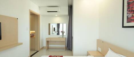 A modern hotel room with a large bed, a bedside table, a desk with a chair, a mirror, and a framed picture on the wall.