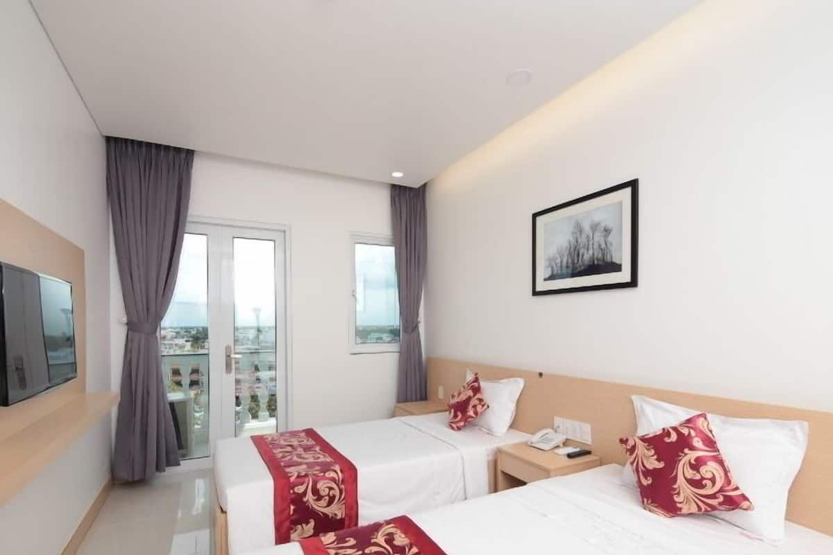 A hotel room with two beds, a TV, a painting, and a balcony with curtains.