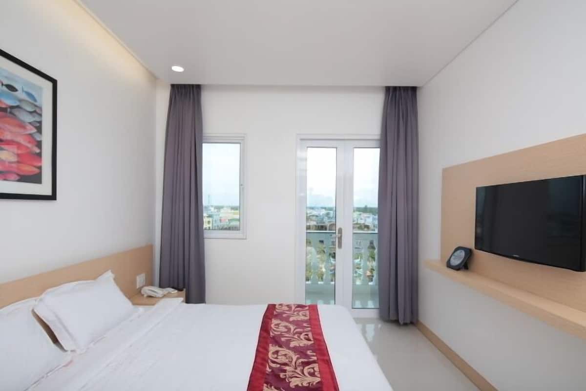 A hotel room with a bed, a TV mounted on the wall, and a balcony with curtains.