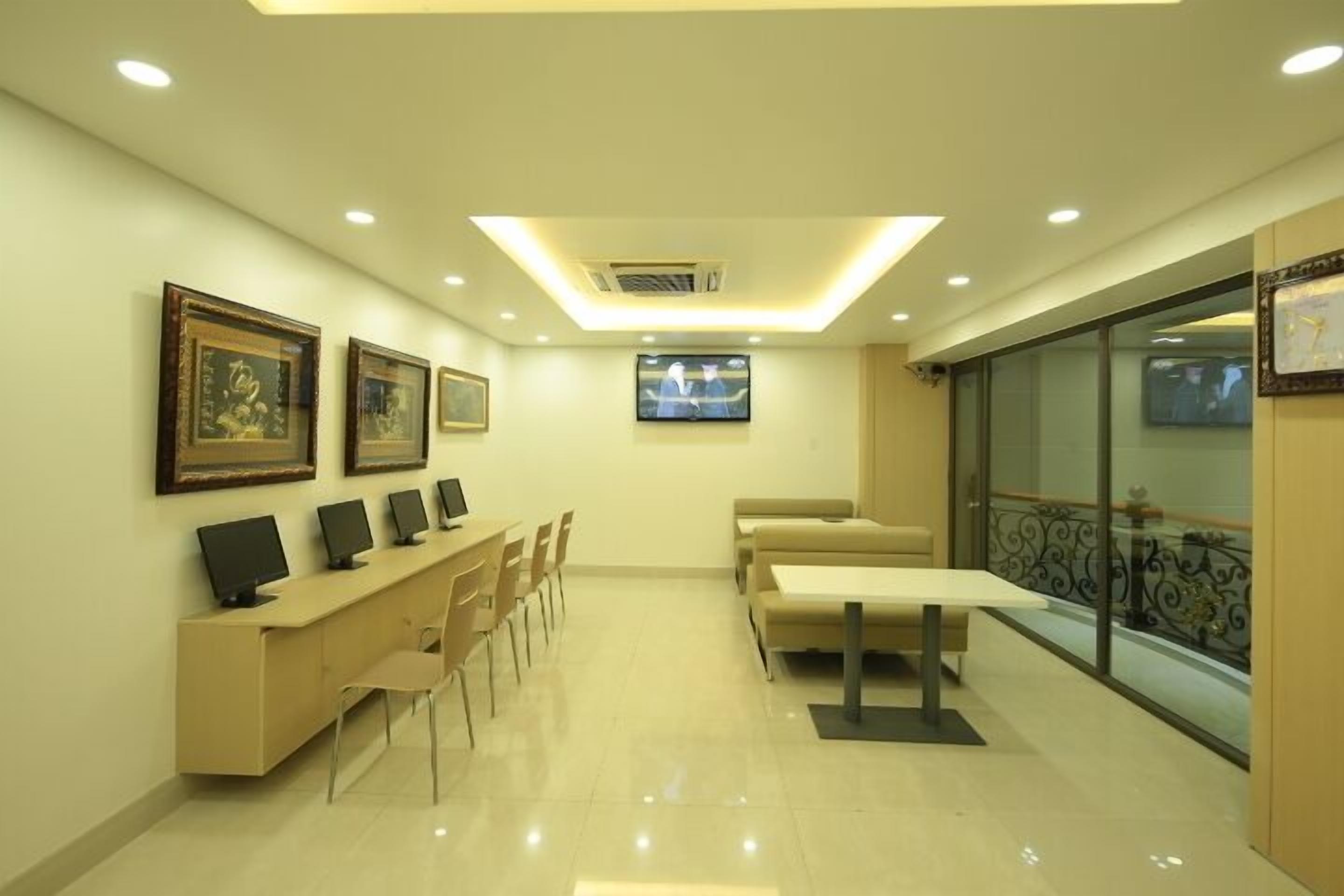 A modern hotel lobby with a reception desk, several chairs, a sofa, and a television screen.