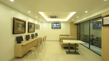 A modern hotel lobby with a reception desk, several chairs, a sofa, and a television screen.