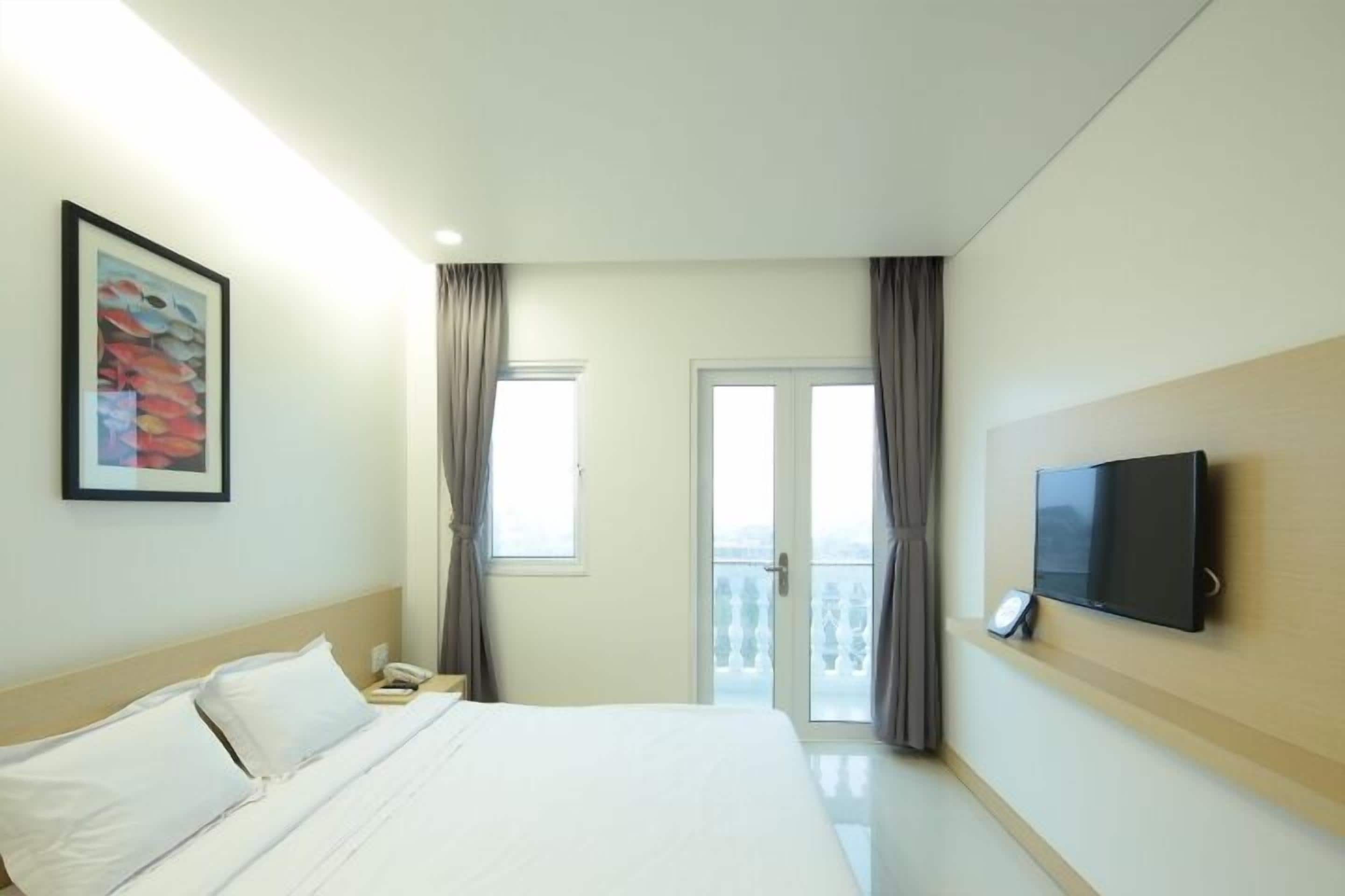 Habitación de hotel con una cama, un televisor de pantalla plana montado en la pared, un cuadro en la pared y una ventana con cortinas.