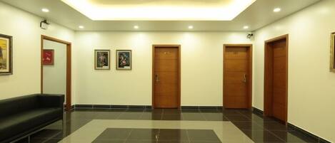 A lobby with a black leather sofa, wooden doors, and framed artwork on the walls.