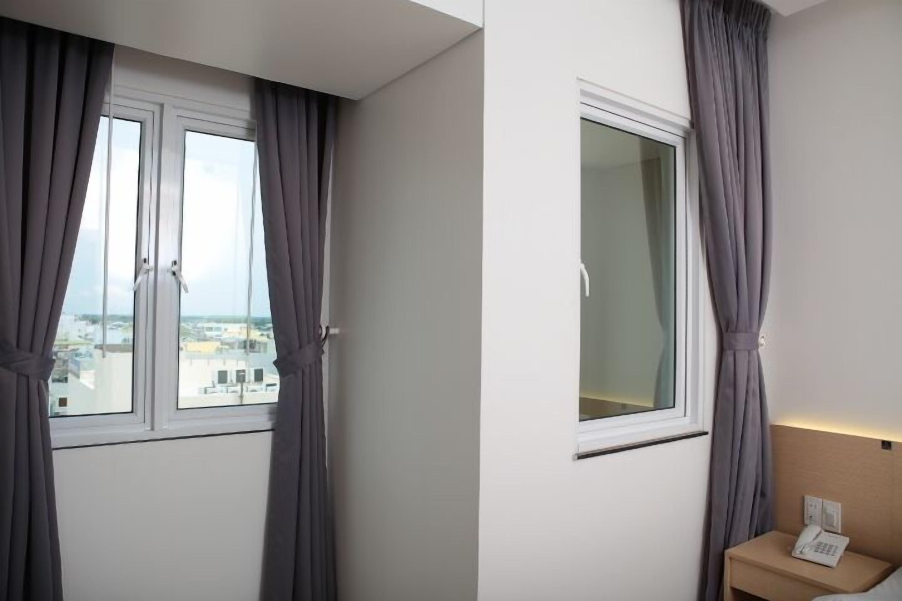 Habitación de hotel con un ventanal amplio, una mesita de noche con teléfono y vistas a la ciudad.