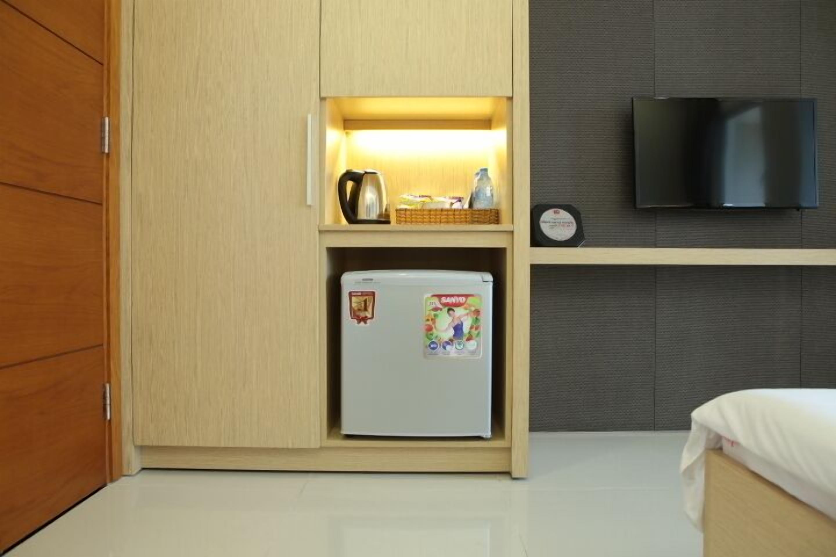 Una habitación compacta con cama, refrigerador pequeño, microondas y televisor montado en la pared.