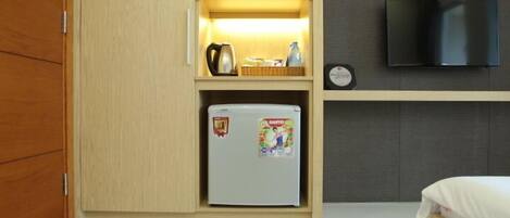 Una habitación compacta con cama, refrigerador pequeño, microondas y televisor montado en la pared.