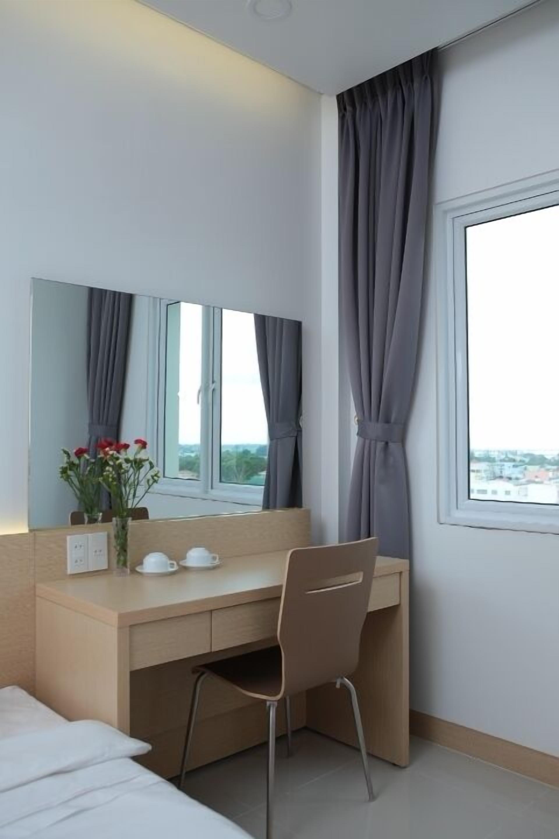 Ein Hotelzimmer mit Bett, Schreibtisch mit Stuhl, Spiegel und einem Fenster mit Vorhängen.