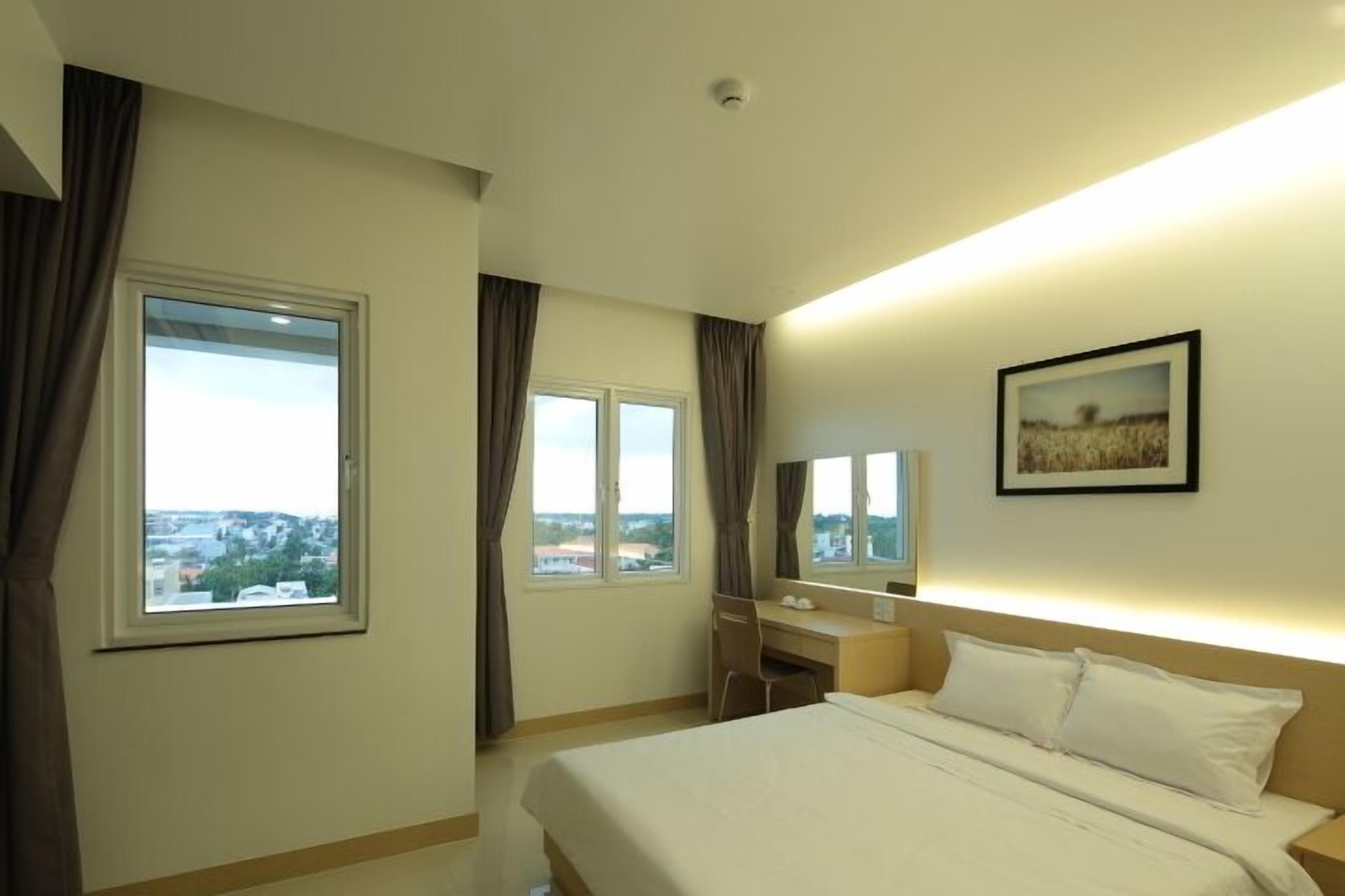 A hotel room with a bed, a desk, and two windows.