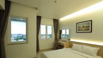 A hotel room with a bed, a desk, and two windows.