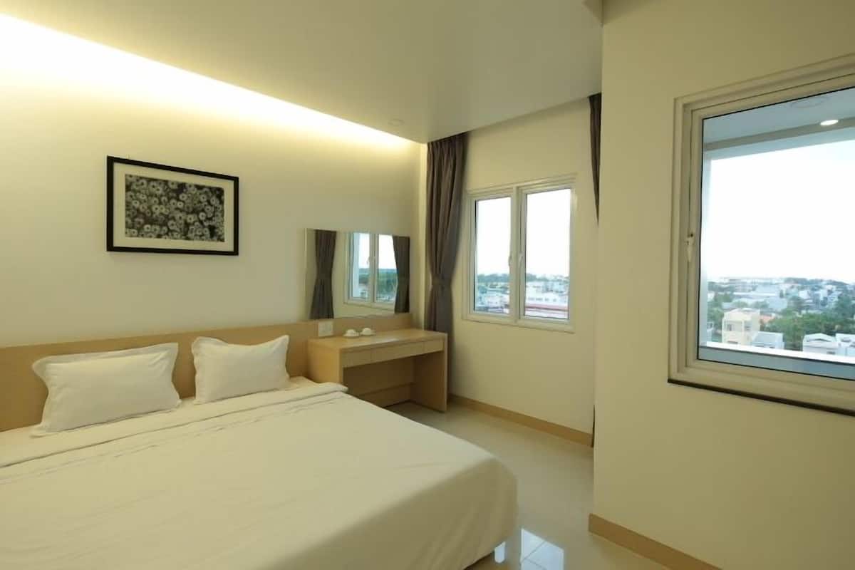 A hotel room with a bed, a bedside table, a mirror, a window with a view, and a framed picture on the wall.