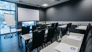 A conference room with a large screen, multiple tables, and chairs. - Q Hotel Kraków (Kraków)