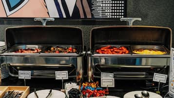 Un bufé con secciones de comida identificadas, que incluye tocino, champiñones fritos, kielbaski, huevos revueltos y cebollín.