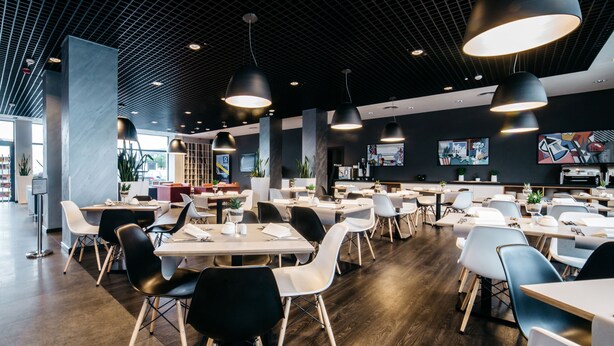 A modern restaurant interior with high ceilings, pendant lighting, and a mix of white and black chairs. - Q Hotel Kraków (Kraków)