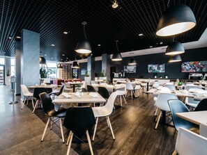 Un interior de restaurante moderno con techos altos, iluminación colgante y una mezcla de sillas blancas y negras.