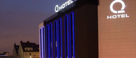 Un edificio de hotel con un llamativo letrero que dice 'Q HOTEL', con detalles de iluminación azul vertical.