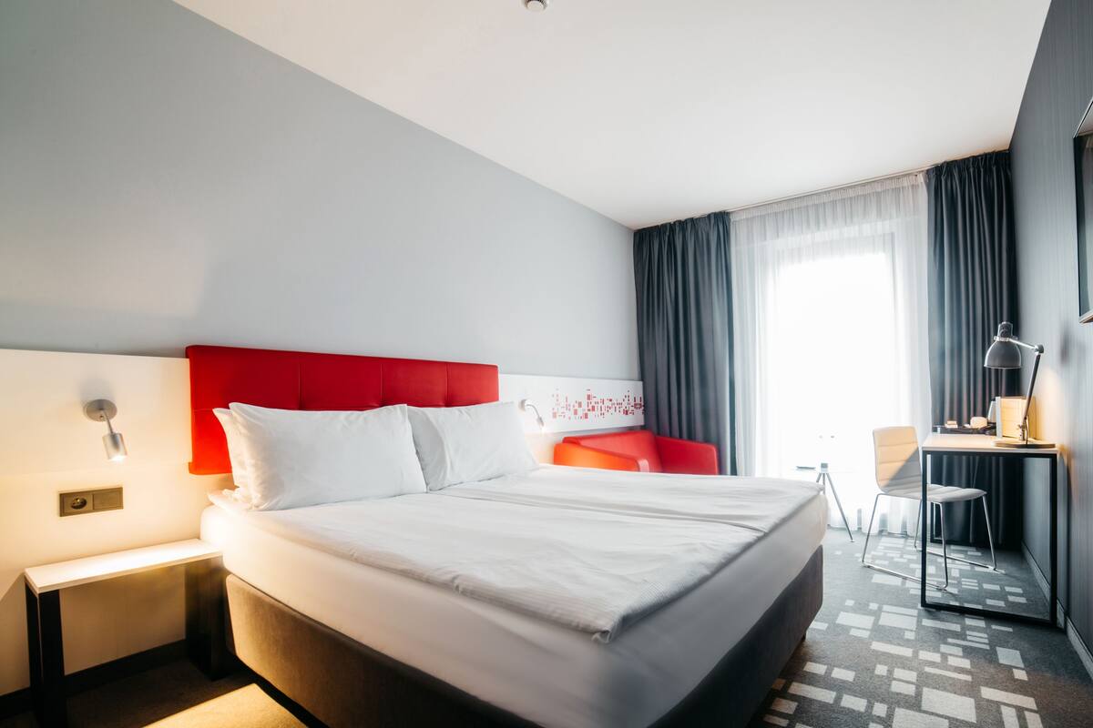 A modern hotel room with a large bed, a desk, a chair, and a red sofa.