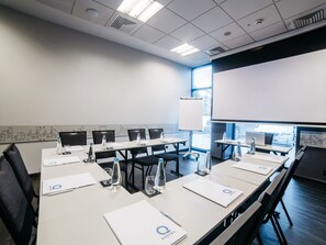 Ein Konferenzraum mit einem langen Tisch, Stühlen, einer Projektionsleinwand und einer Tafel.
