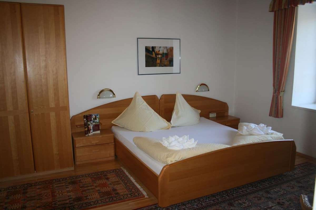 A hotel room with a wooden bed, two bedside tables, a nightstand, a wall-mounted picture, and a window with curtains.