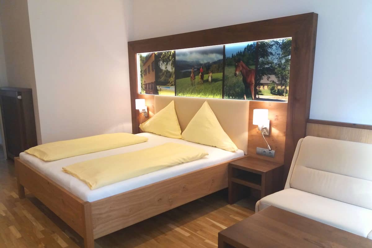 A bedroom with a wooden bed, two pillows, a nightstand, a bedside table, and a wall-mounted picture.