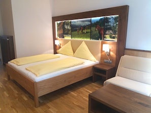 A bedroom with a wooden bed, two pillows, a nightstand, a bedside table, and a wall-mounted picture.