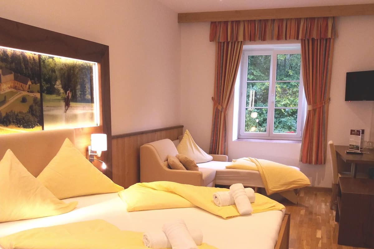 A hotel room with a large bed, a sofa, a desk, and a window with curtains.