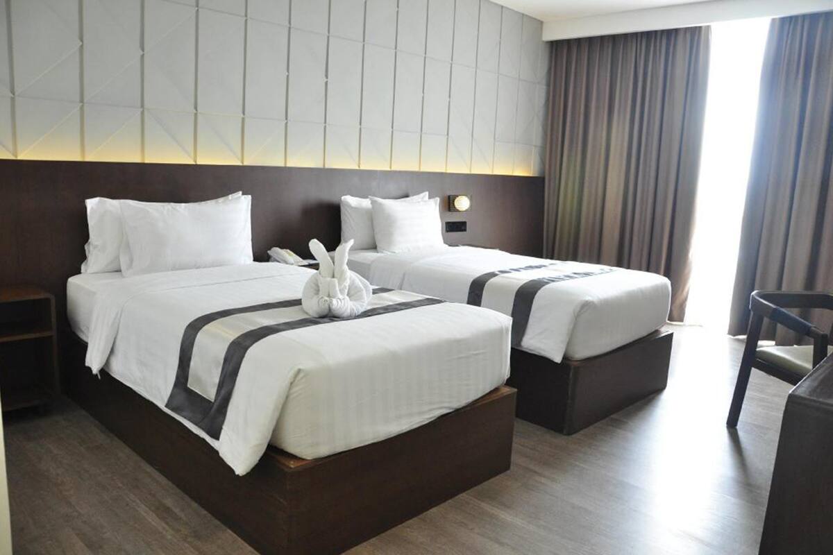 A hotel room with two beds, a nightstand, a desk, and a chair.
