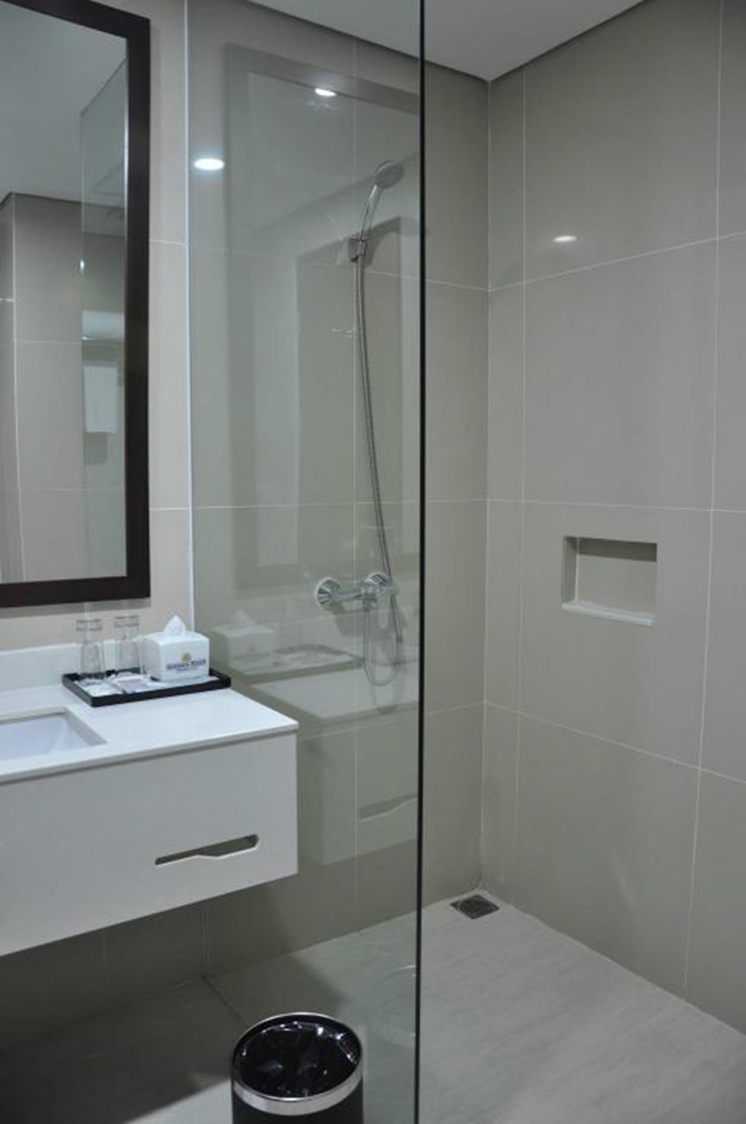 A modern bathroom with a glass shower enclosure, a white sink with a mirror, and a trash bin.