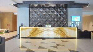 Un espace d’accueil d’hôtel avec un comptoir en marbre, un bureau pour le responsable de service et un téléviseur fixé au mur.
