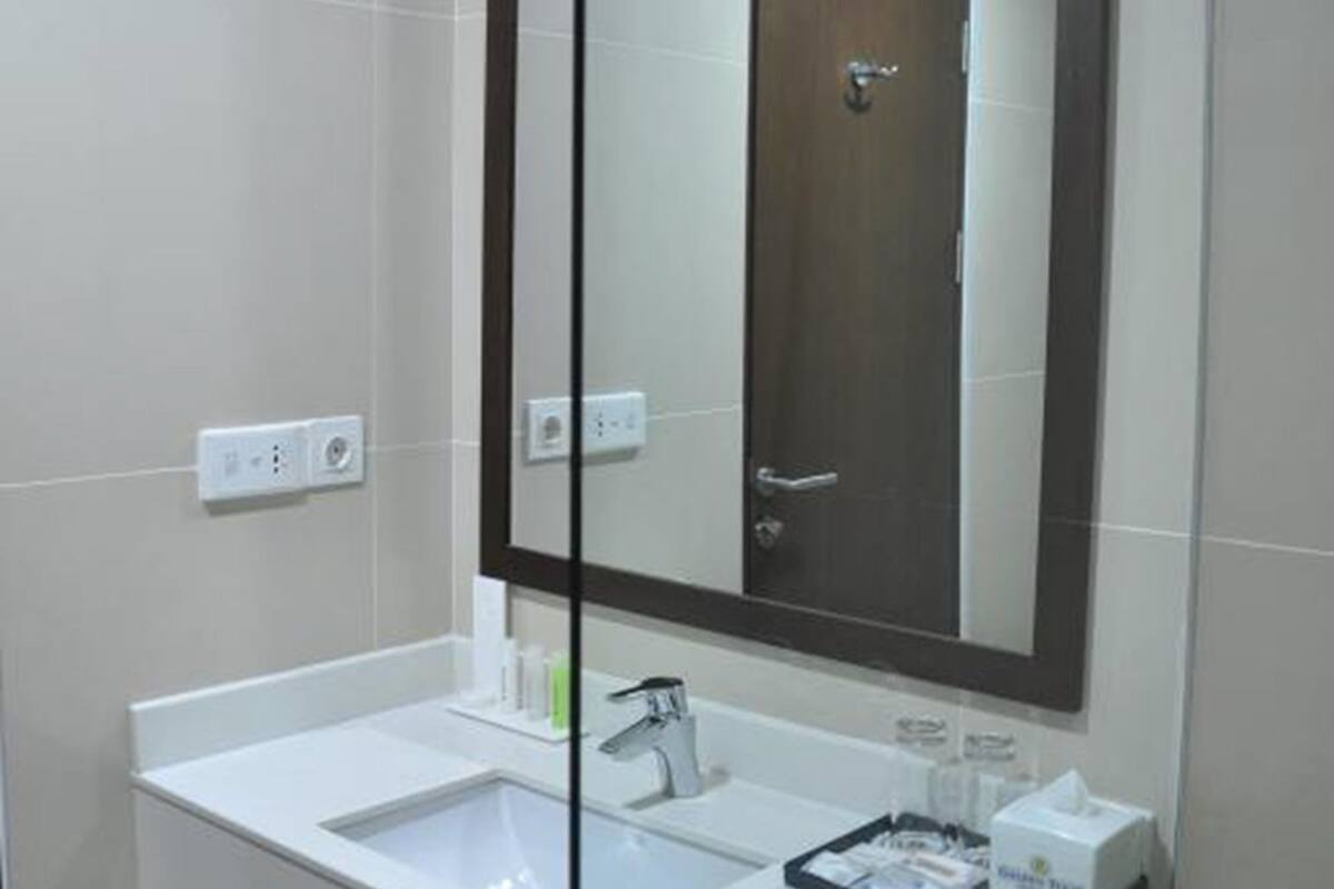 A modern bathroom with a white sink, a large mirror, and a door visible in the reflection.