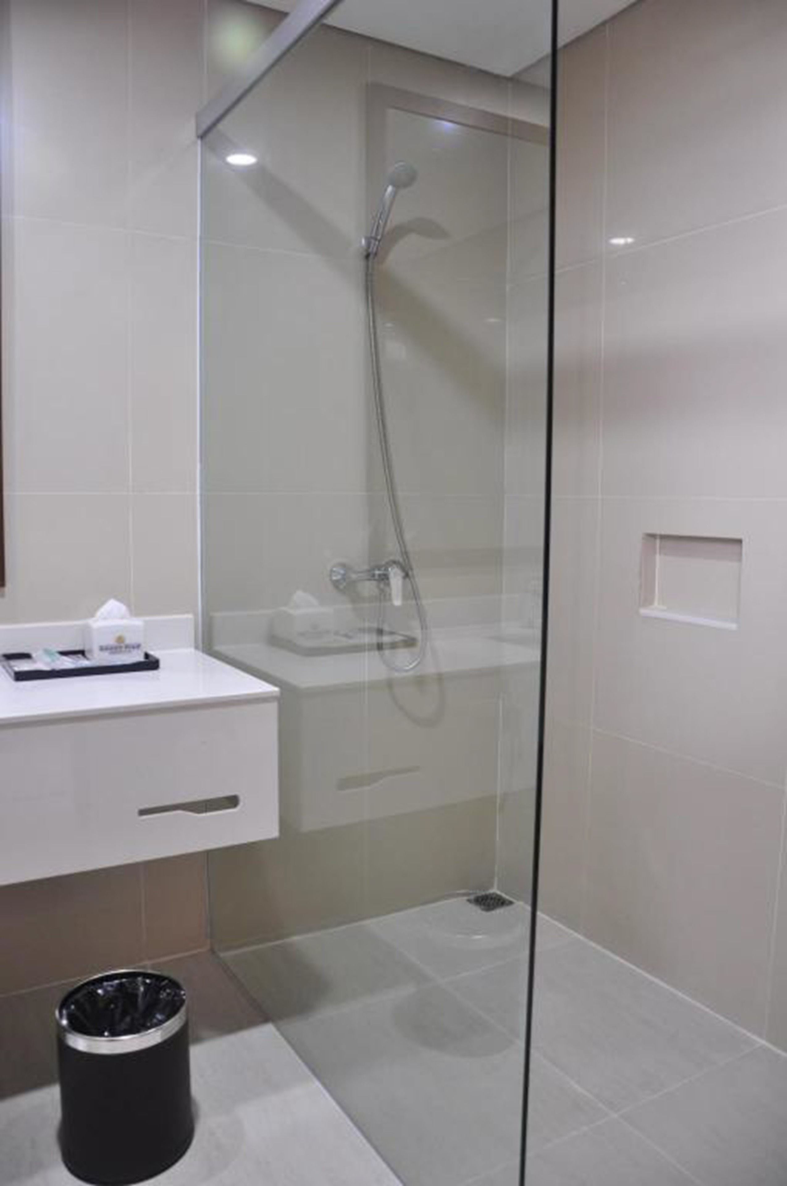 A modern bathroom with a glass-enclosed shower, a white sink, and a trash bin.
