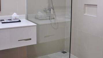 Un baño moderno con ducha de vidrio, lavamanos blanco y un cubo de basura.