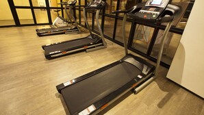 Une salle de sport équipée de tapis de course, de vélos d’exercice et d’un mur recouvert de miroirs.
