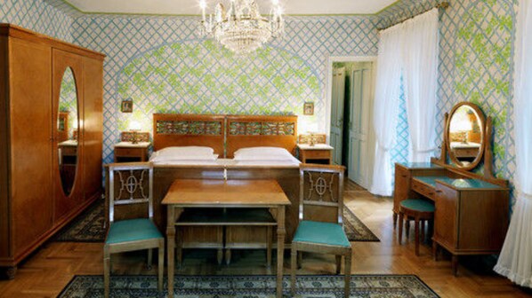 A bedroom with a large bed, two bedside tables, a wooden dresser, a desk with a chair, and a mirror. - Hotel de la Poste (Cortina d'Ampezzo)