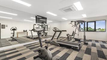 Un gimnasio con máquinas de cardio, un espejo grande y un ventanal con vistas.