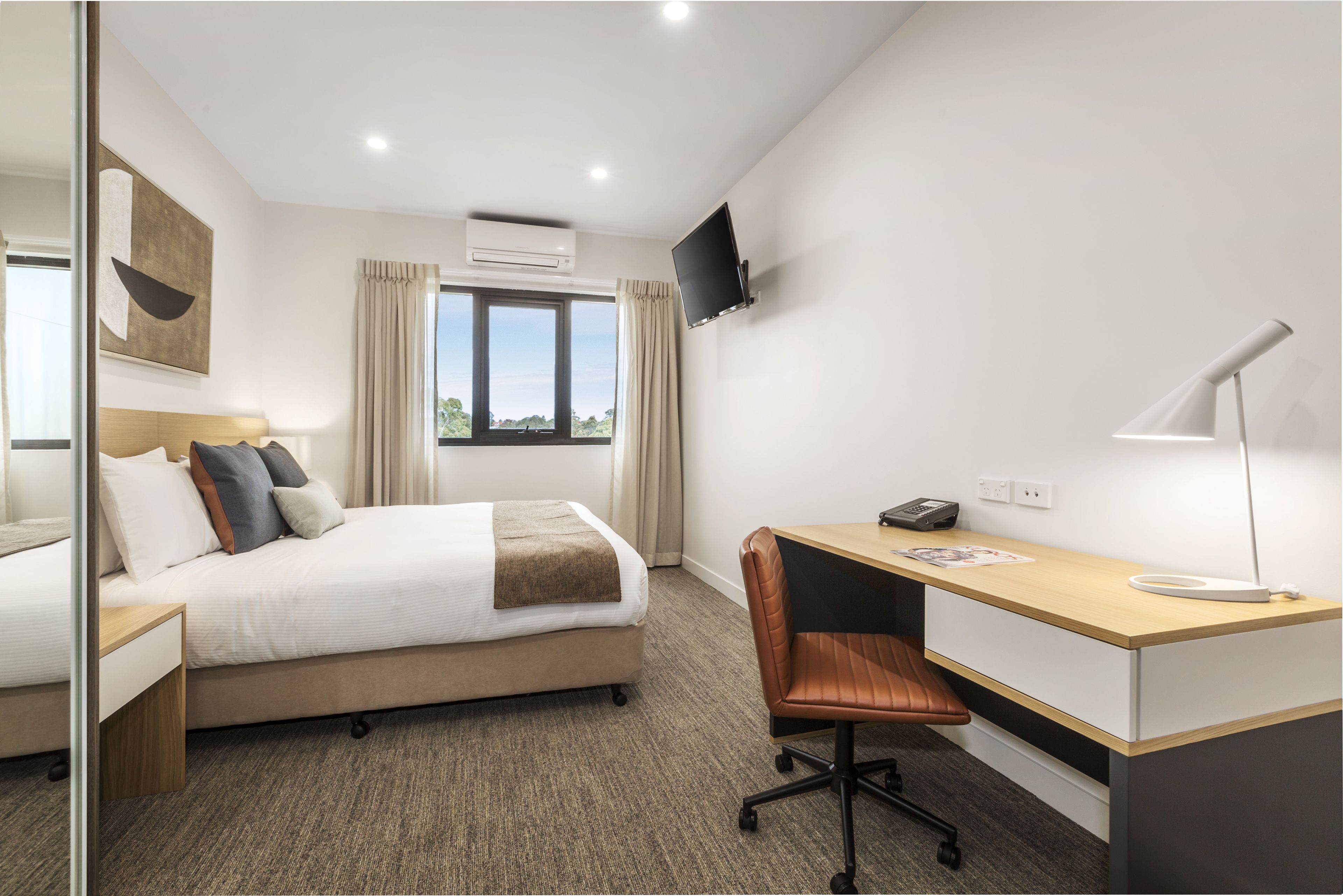 A hotel room with a bed, desk, chair, and a TV mounted on the wall.
